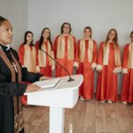 A pastor delivers a sermon at a podium with a choir standing behind.
